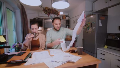 Sad young couple paying the bills. Man and woman sitting in the kitchen and sorting checks and accounts.