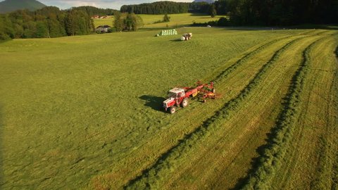 Aerial of tractor makes hay bales and drops them covered in plastic on sunny day in the mountains of Austria 4K