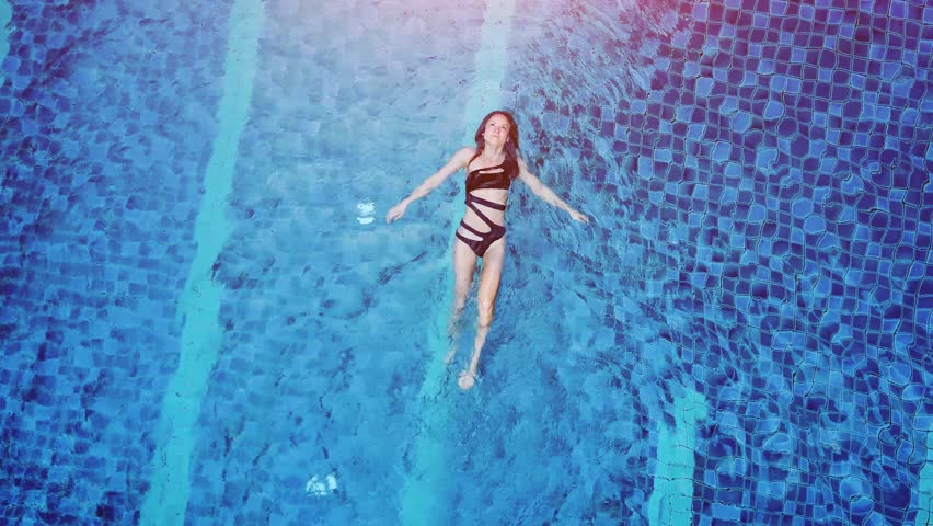 Top view aerial photo of a seductive sexy model in black swimwear is enjoying relax in hotel pool. Amazing fashion woman in bikini having luxury spa rest | Shutterstock HD Video #24674642