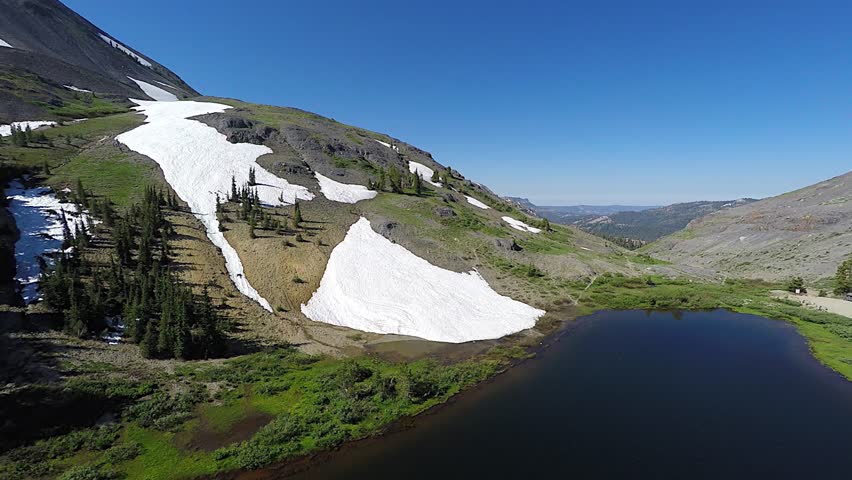 4k UHD Aerial tracking back from snow capped mountain with calm mountain lake below in Arnold California in the Yosemite National Park as camera tracks away from mountain