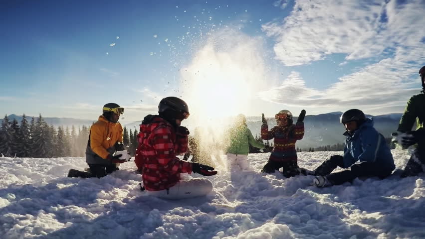Happy group of skiers having fun sitting in snowdrift with snowboards and tossing snow