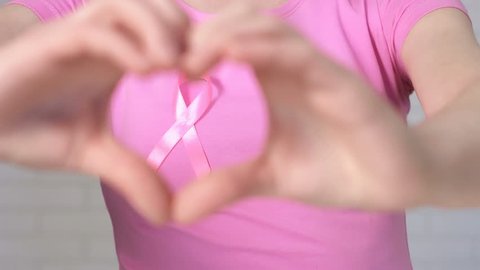 Woman showing heart sign framing breast cancer awareness ribbon - breast cancer awareness concept
