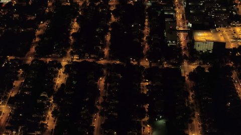 AERIAL HELI SHOT: Flying above the roofs of residential luxury houses in suburban neighborhood lit up with lights at night in metropolis of new York City. Urban street grid and cityscape of NY suburbs