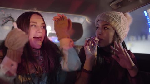 Young Women Celebrate In Backseat Of Moving Car, They Dance And Sing And Blow Party Blowers ஸ்டாக் வீடியோ