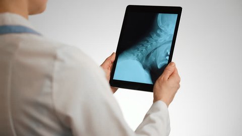 Woman radiologist analyzing patient's cervical x-ray on digital screen.