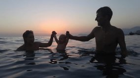 Mother and father hold baby on hands, touch his lips and smile on sunset in Mediterranean Sea, mobile phone video.