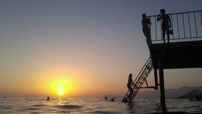 Silhouettes of unrecognized people in water and on pier on sunset in Mediterranean Sea, mobile phone video.