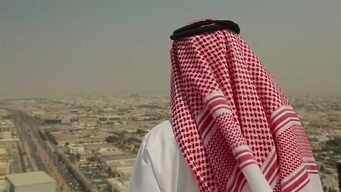 Mid shot of a Saudi Arabian man in local dress standing on a roof looking out across the city of Jeddah, in Saudi Arabia in the Middle East on a windy day.