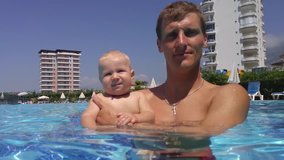 Father hold baby on hands in swimming pool near hotels at sunny day, mobile phone video.