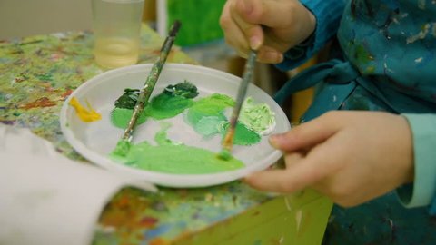 Children's hands close-up are mixed by a brush of different colors of paint. School of drawing, young artist