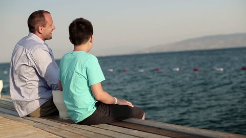 Father with teenage son sitting on wooden pier by the sea
 Video de stock