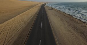 Aerial and bird perspective view from drone of Namibian Atlantic coastline, lone road along the coast, beach, surf break point and landscape with ocean background of sand dunes at Namibia's west coast