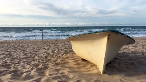 Slow motion, wavy Mediterranean beach and rowboat on sunset evening time in Skikda, Algeria.