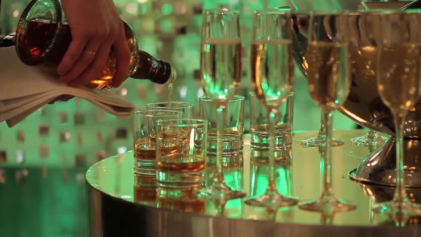 Glasses on the buffet table, pour whiskey in glasses, the hall of a restaurant or hotel, the interior is dark, the waiter pours whiskey into glasses, champagne in glasses on the table