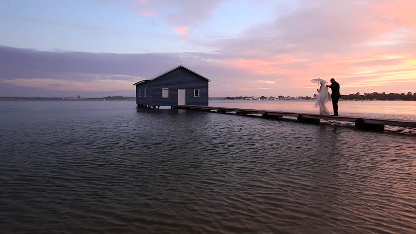 A couple dressed in wedding attire walks along the jetty on sunset at the Crawley Boatshed on Mounts Bay Road, Perth, Western Australia.