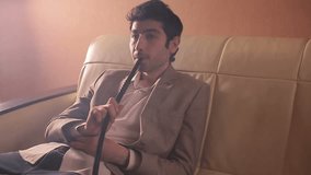 Businessman smoking a hookah and relaxing on a sofa in cozy room. Video full hd.