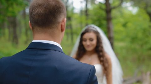 Bride and groom pose in the wood. Young man and woman gently look at each other.Beautiful background. Happy moment of loving couple.