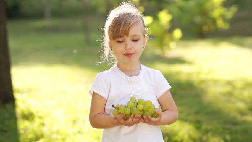 Girl eating grapes and looking at camera outdoors