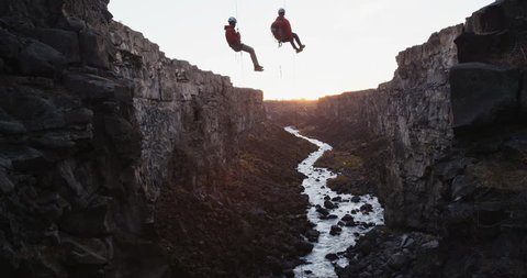 Slow reveal of two rock climbers hanging off of ropers above a river in a canyon