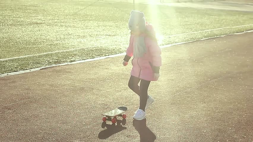 Pretty little girl learning to skateboard outdoors on beautiful summer day. Fashionably dressed girl, learn to skateboard on the stadium
