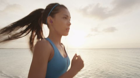 Female runner running on beach - summer vacations exercise. Asian female athlete on holiday travel working out her cardio listening to music in earphones. REAL TIME, RED EPIC.