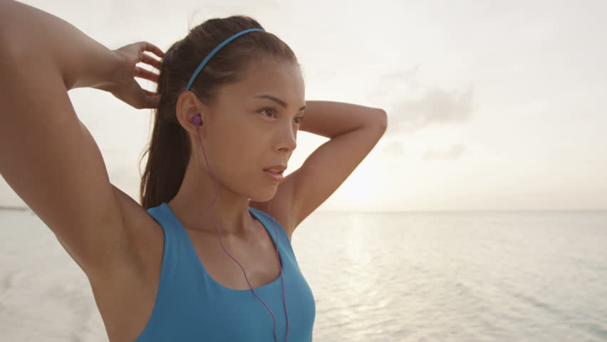 Runner woman getting ready to run and starts running on beach at sunset wearing earphones listening to music. STEADICAM SLOW MOTION, RED EPIC. Royalty-Free Stock Footage #24779204