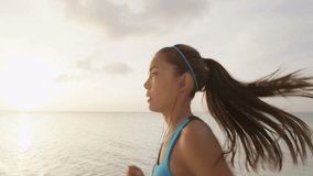 Determined female runner jogging at beach during sunset. Sporty young woman is listening music through earphones against sky wearing blue sports bra. SLOW MOTION, STEADICAM, RED EPIC.