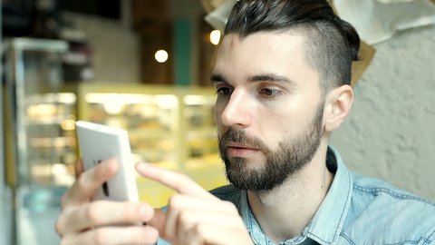 Handsome man with mun bun looks shockes and worried while checking news on smartphone
