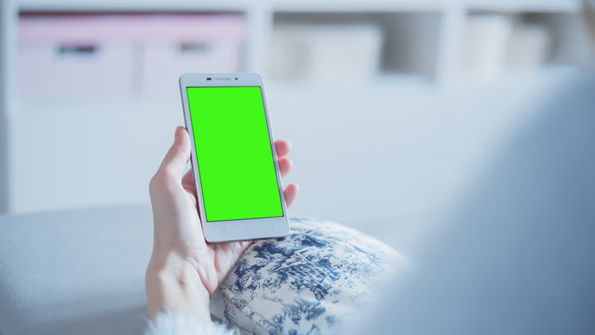 Young Woman sitting on a couch uses SmartPhone with pre-keyed green screen. Few types of motion - scrolling up and down, tapping, zoom in and out. Perfect for screen compositing. 10bit ProRes 444. Royalty-Free Stock Footage #24787382