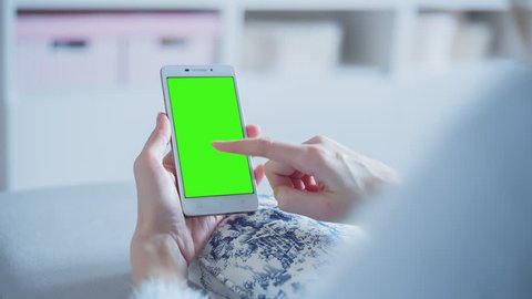 Young Woman sitting on a couch uses SmartPhone with pre-keyed green screen. Few types of motion - scrolling up and down, tapping, zoom in and out. Perfect for screen compositing. 10bit ProRes 444.