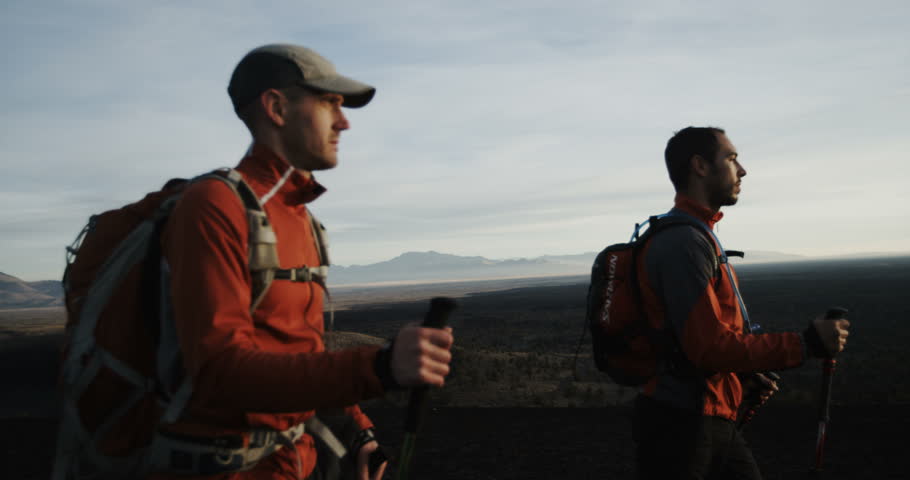 Teammates hiking towards the sunrise with orange jackets slow motion