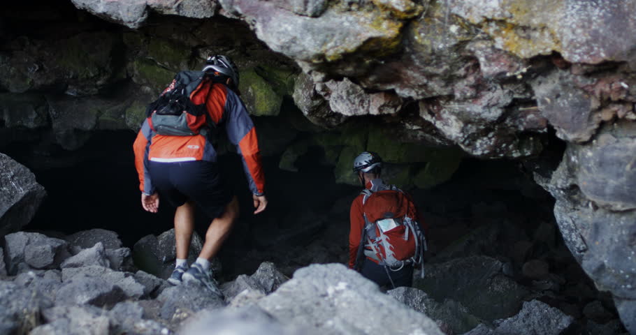 Two spelunkers walk into a dark cave in slow motion slider