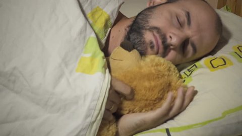 Adult male sleeping and hugging teddy bear.