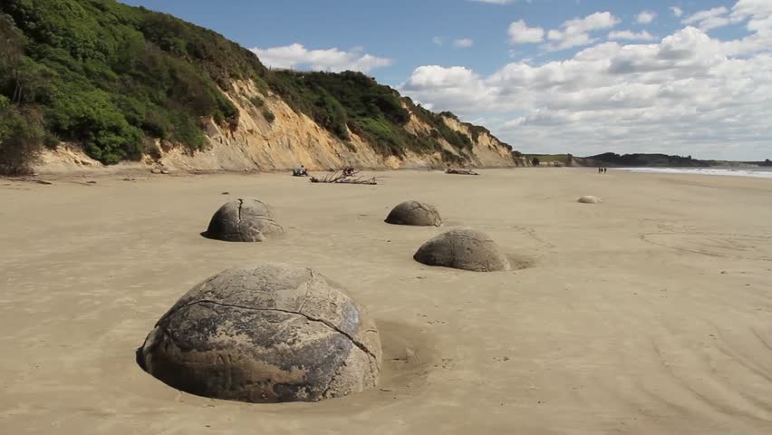 Perfectly round boulders on sandy beach with dunes and vegetation, moeraki, new zealand