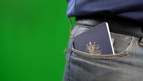 Man removing Australian passport from jeans pocket close up against green screen.