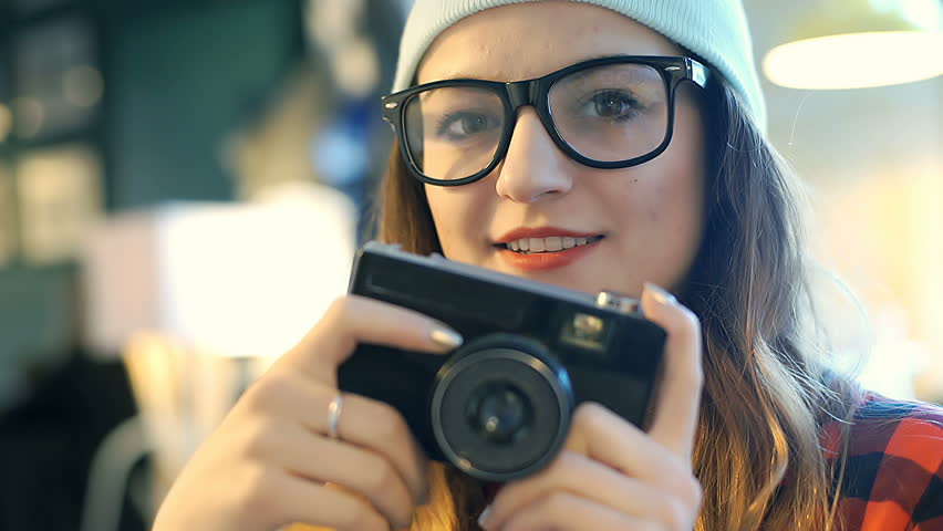 Brunette is holding vintage camera and smiling while sitting in the cafe
