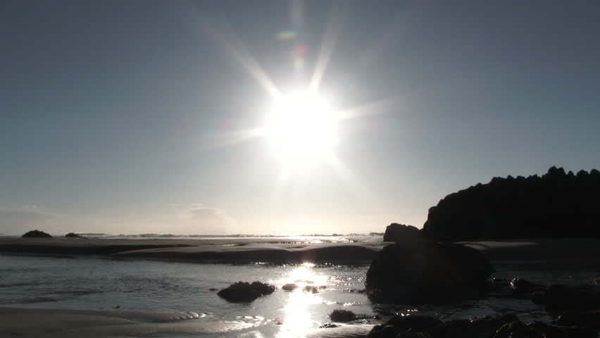 Two silhouetted people walking along ocean coastline on calm and clear evening in Oregon.
