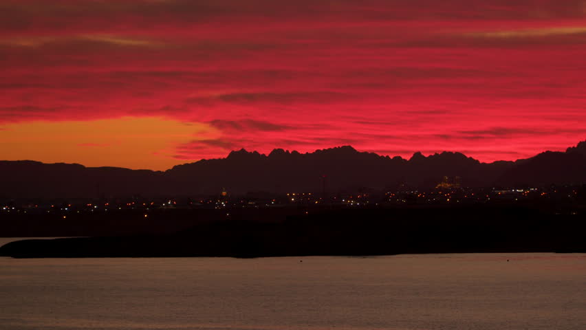 City by the sea against the sky at sunset. On the horizon there are mountains