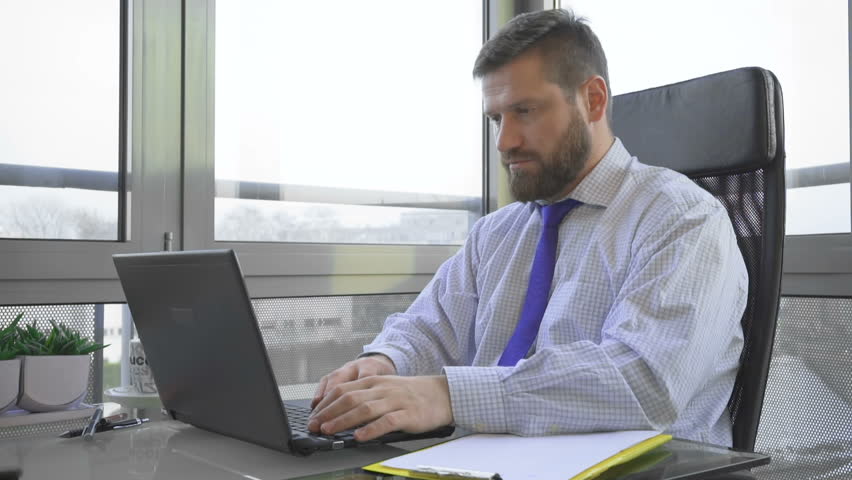 Businessman working, writing on laptop computer looking at camera, in office Royalty-Free Stock Footage #24849638