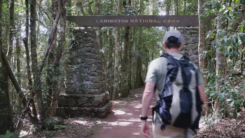 a hiker walks under a sign at lamington national park in queensland, australia