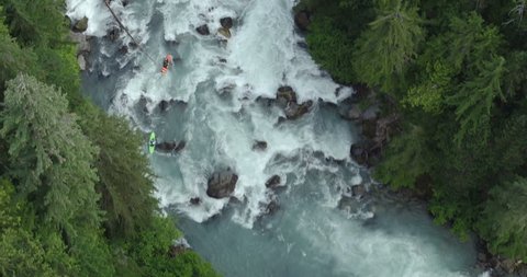 Aerial - Two kayakers paddling down blue river waterfall rapids with trees - Pacific Northwest BC
