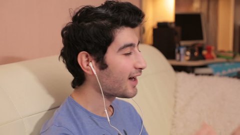 Young man with headphones listening to music at room. Video full hd side view.