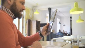 Man taking video call on internet app, by tablet, in cafe, close profile shot