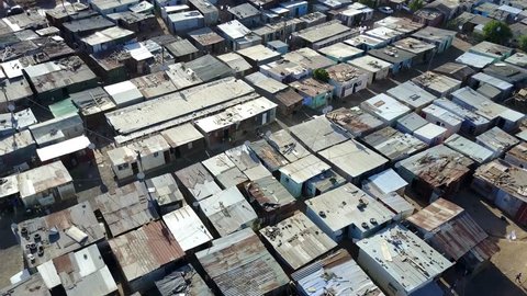 Aerial bird view view of slum a heavily populated urban informal settlement characterized by substandard housing and squalor showing people walking through streets and rusty metal home roof tops 4k