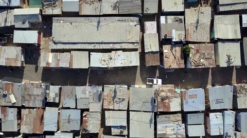 Aerial top-down view of slum a heavily populated urban informal settlement characterized by substandard housing and squalor showing people walking through streets and rusty metal home roof tops 4k