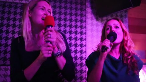 Two joyful women singing and dancing in karaoke club
