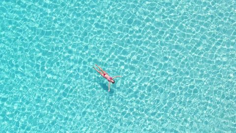 Aerial view of an attractive woman in a red bikini floating in crystal clear sea