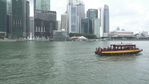Singapore, Singapore - February 22, 2017: Follow pan of a tourist boat full of tourists at the Marina Bay in Singapore. Skyscrapers of the Central Business District visible in the background.
