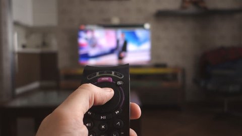 Male hand holding the TV remote control and turn off smart tv. Channel surfing, focused on the hand and remote control. Internet TV.