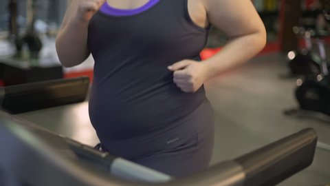Fat young woman running on treadmill, working out hard to lose excess weight, personal training program. Obese female doing sport exercise in gym, fitness endurance. Physical activity, motivation
